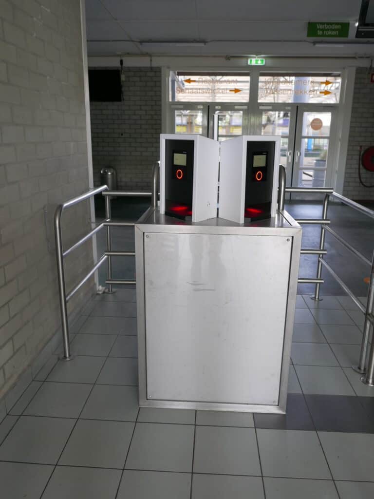 Foto van de toegangshekjes (tourniquets) in de entreehal van de IJsbaan Haarlem. De QR-code op de online kaartjes kun je hier scannen. Magneetpassen en abonnementen scan hier door die tegen de rode cirkel te houden. Met online kaartje hoef je niet in de rij voor de kasabalie te wachten en kun je direct naar het ijs doorlopen.